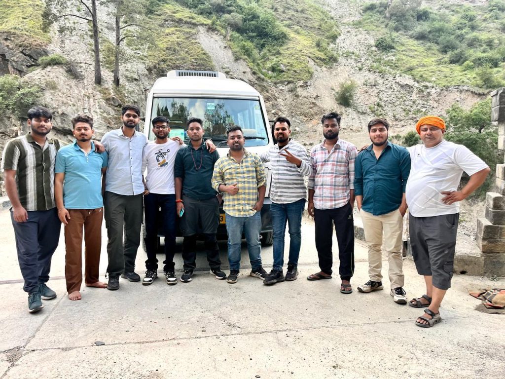 Travelers posing in a line in front of a Tempo Traveller in the hills
